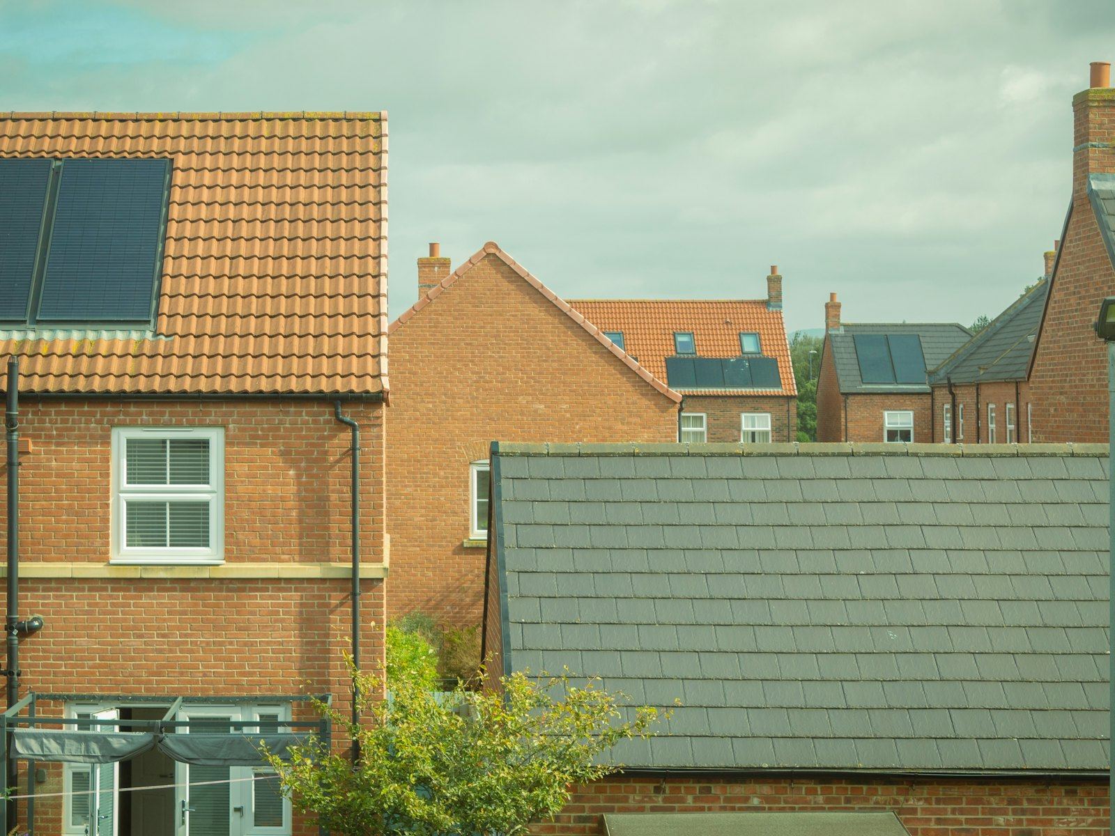 Suburban brick houses with solar panels and tiled roofs under a cloudy sky.